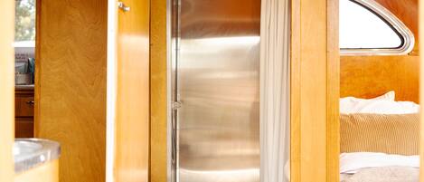 A compact bathroom with a toilet and shower area, wooden walls, and a window.