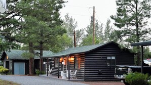 Une cabane en rondins avec un porche couvert, une allée en gravier et un camion garé.