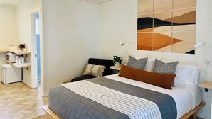 Une chambre à coucher moderne, avec un lit, des tables de chevet, un bureau et un grand tableau abstrait accroché au mur.