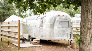 A vintage trailer with a wooden bench and steps leading up to it, parked in a wooded area. - This is Cliffy! Our 1967 airstream (Pinetop)