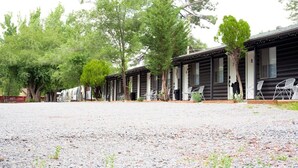 A row of log cabin-style cabins with outdoor seating and trees in the background. - This is Cliffy! Our 1967 airstream (Pinetop)
