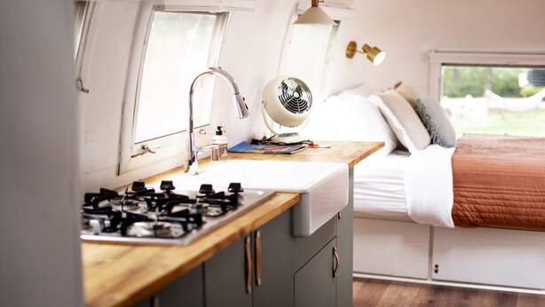 A compact kitchen with a gas stove, a sink, and a fan. - This is Cliffy! Our 1967 airstream (Pinetop)