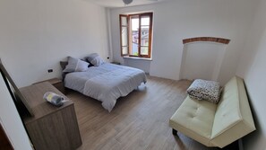 Un dormitorio con cama, mesita de noche, ventana y sofá.