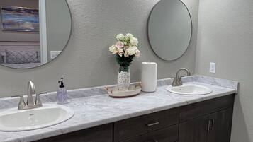 Un baño con lavamanos doble, armarios de madera oscura, un espejo redondo y un florero con flores.