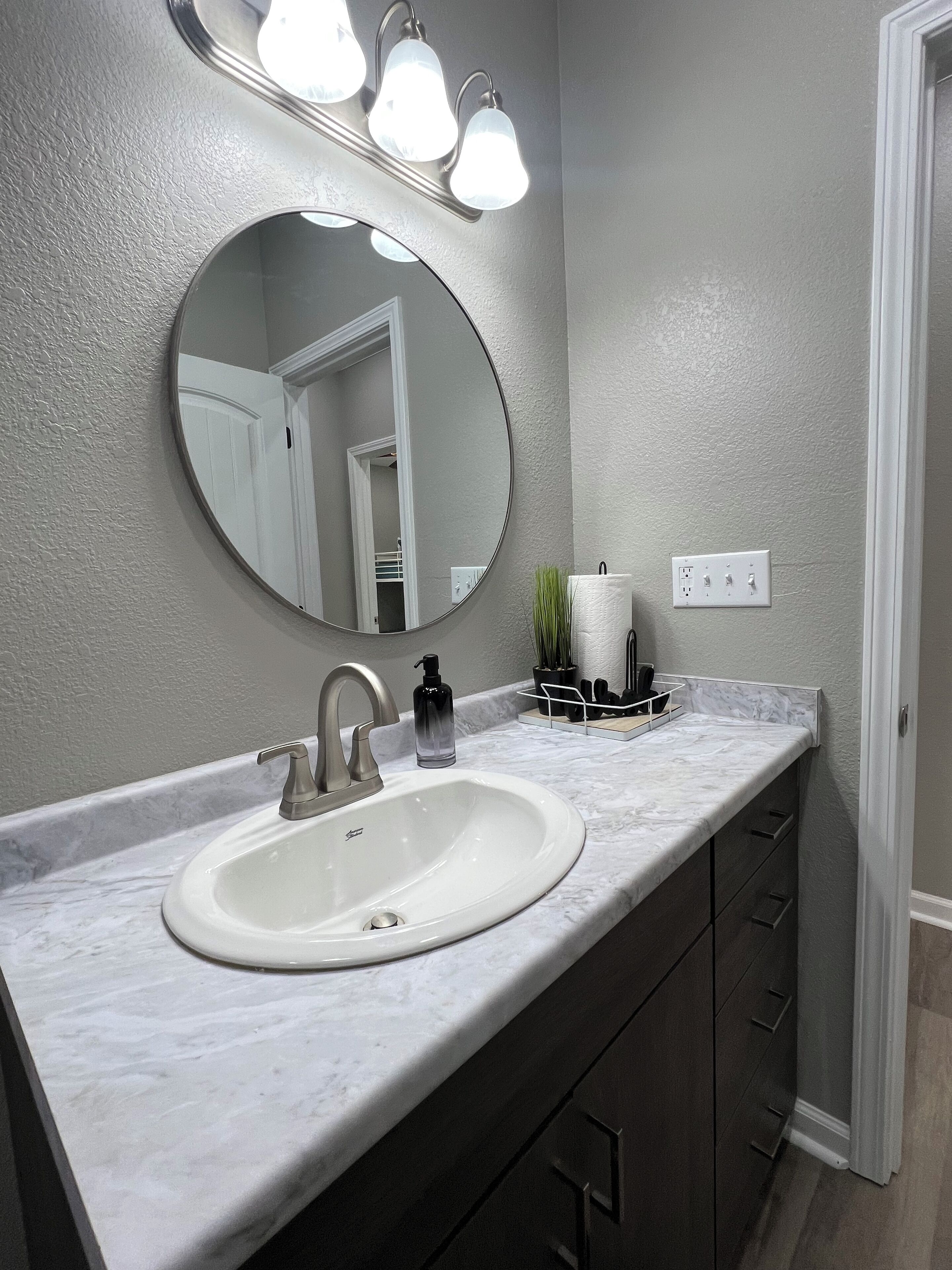 A bathroom with a white sink, a round mirror, and a light fixture above the mirror.