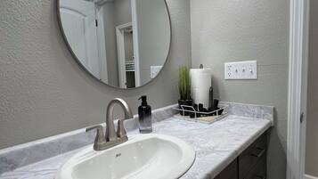 A bathroom with a white sink, a round mirror, and a light fixture above the mirror.
