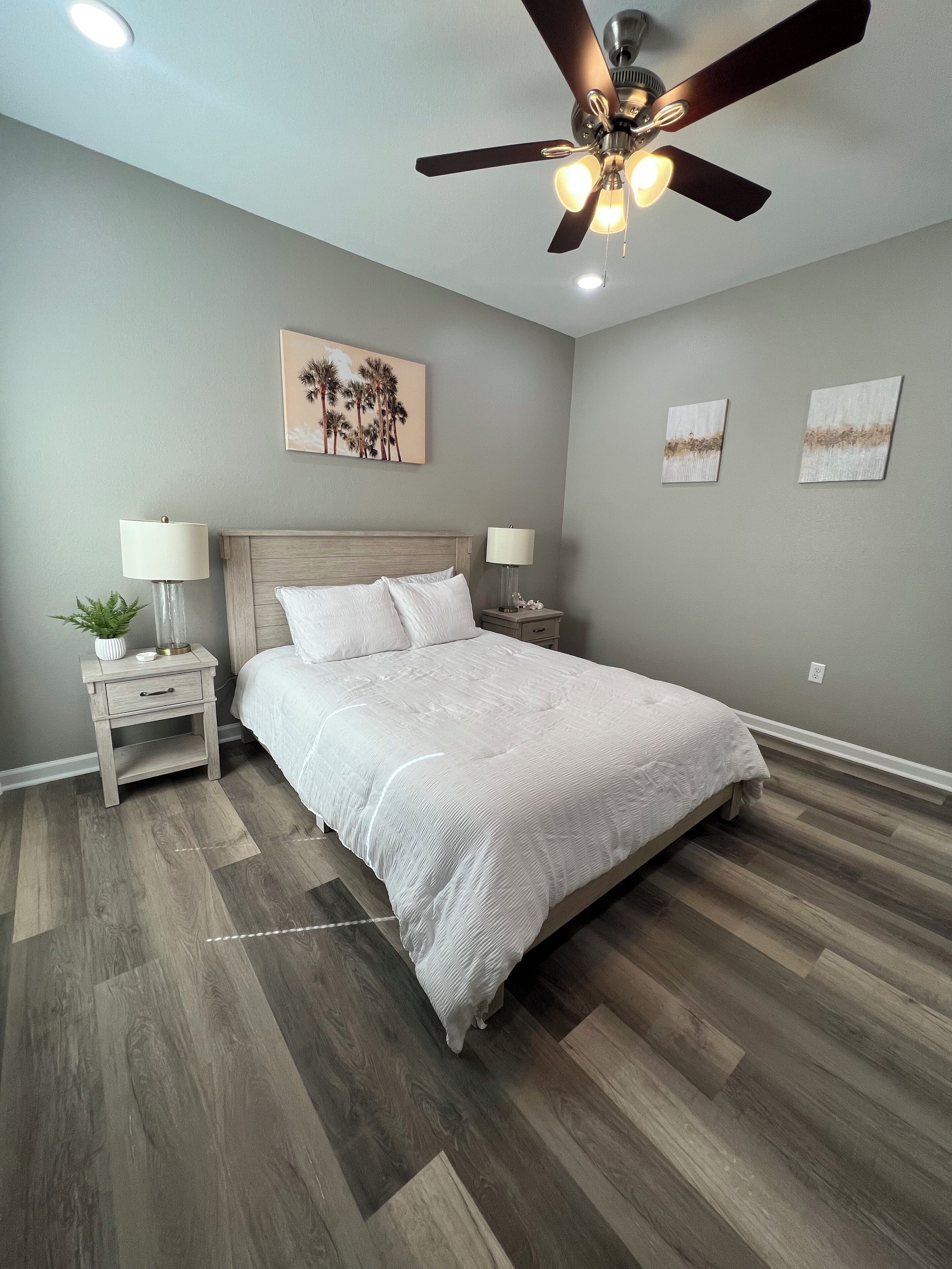 Un dormitorio con cama, dos mesitas de noche, un ventilador de techo y decoración en la pared.