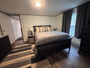 A bedroom with a bed, bedside tables, a dresser, a rug, and a window with curtains.