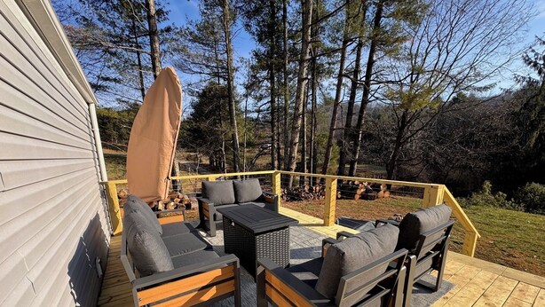 A deck with outdoor furniture, including sofas and a table, surrounded by a wooden railing and a covered area. - Charming Mountain Retreat Near Grayson Highlands, 2BR 2BA, Sleeps 6 (Mouth of Wilson)