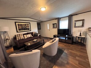 A modern living room with a sofa, armchair, coffee table, TV, and artwork on the wall.