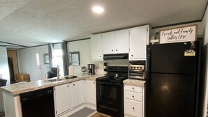 A compact kitchen with white cabinets, a black refrigerator, and a wooden floor. - Charming Mountain Retreat Near Grayson Highlands, 2BR 2BA, Sleeps 6 (Mouth of Wilson)