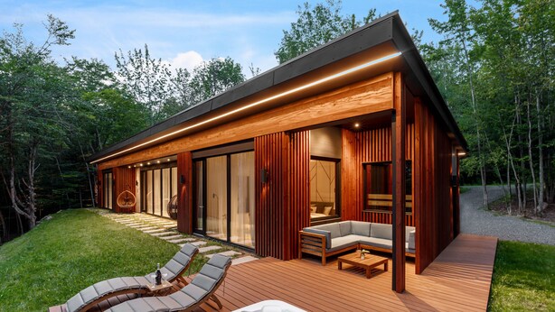 Une cabane moderne en bois, dotée d’une terrasse, de chaises longues et d’un bain à remous.