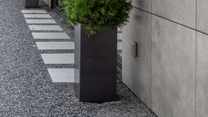 Un bâtiment moderne avec une façade en béton, des poutres en bois et deux arbres à feuilles persistantes plantés dans des pots.