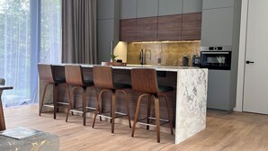 Une cuisine moderne dotée d’un îlot en marbre, de tabourets de bar en bois et d’un four encastré.