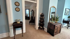 Een kamer met een houten bureau, een dressoir en een spiegel. Er is een deur die leidt naar een andere kamer.