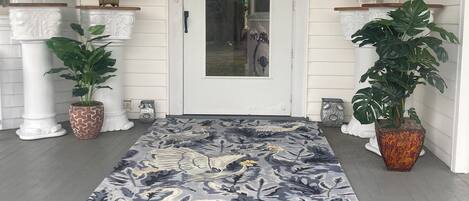 A front porch with a decorative rug, potted plants, and a white door.