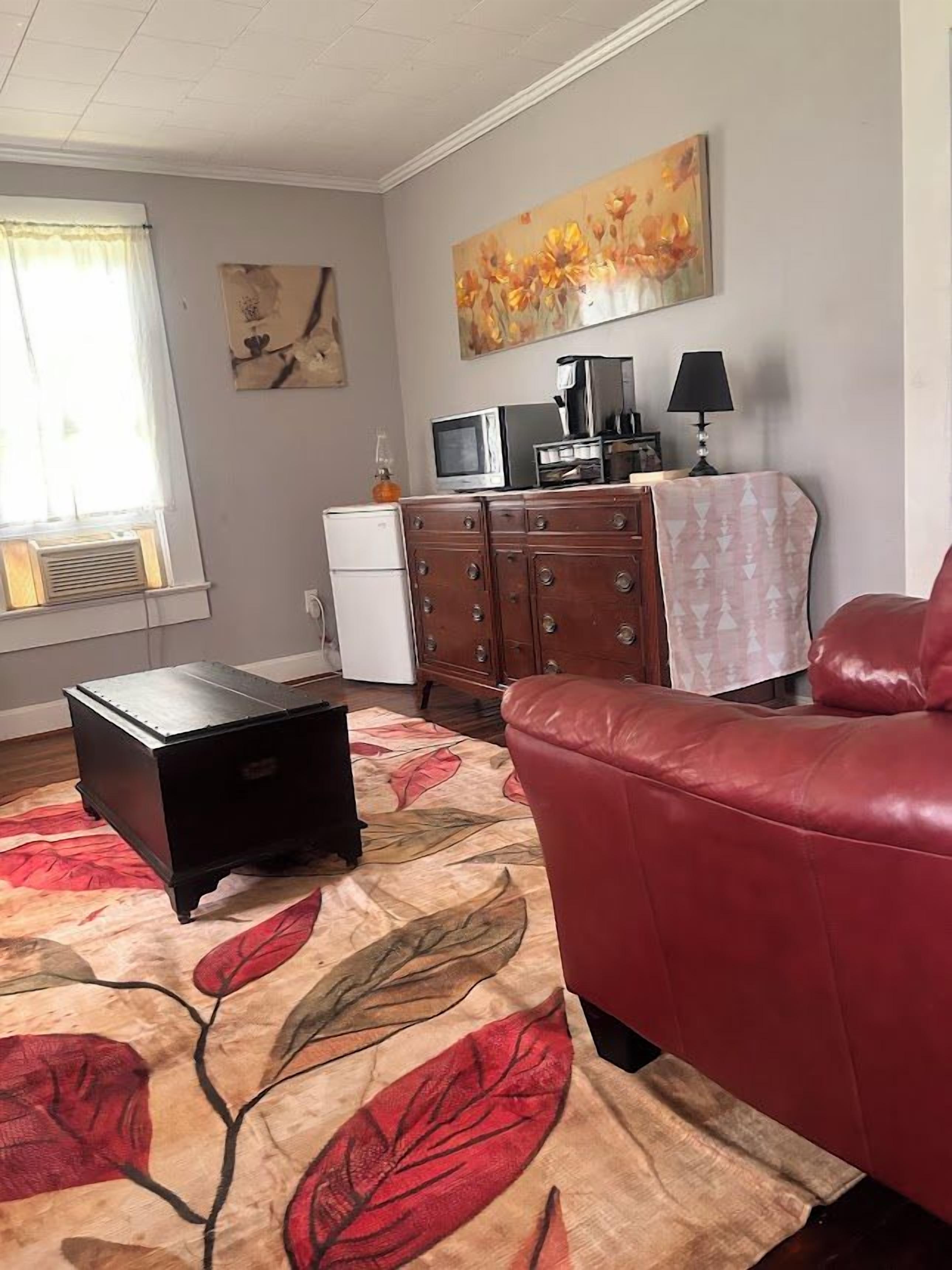 Una sala de estar con un sofá de cuero rojo, una mesa de centro negra, un televisor, un refrigerador y un cuadro en la pared.