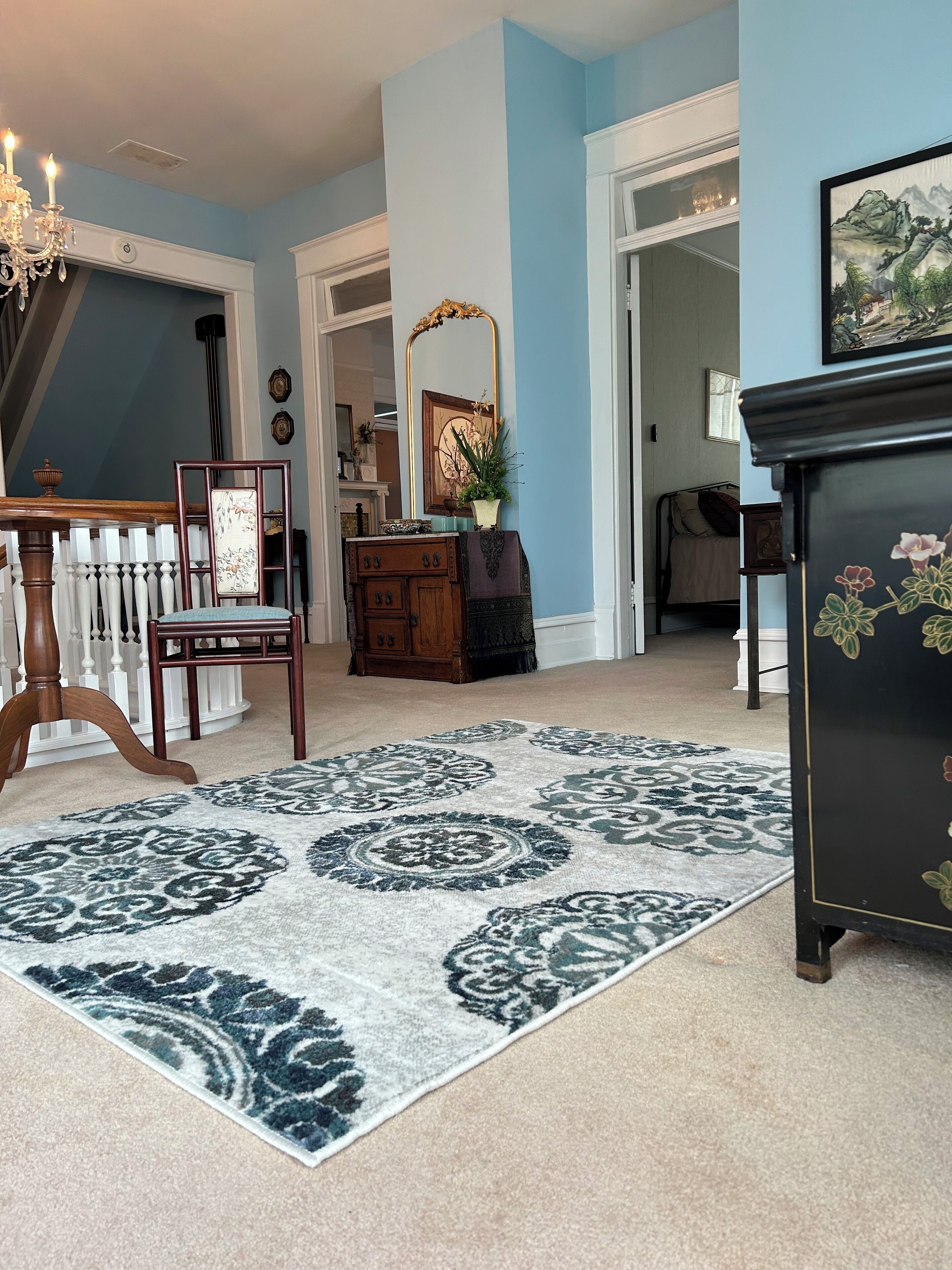 A room with a patterned rug, a wooden chair, a dresser, and a mirror.