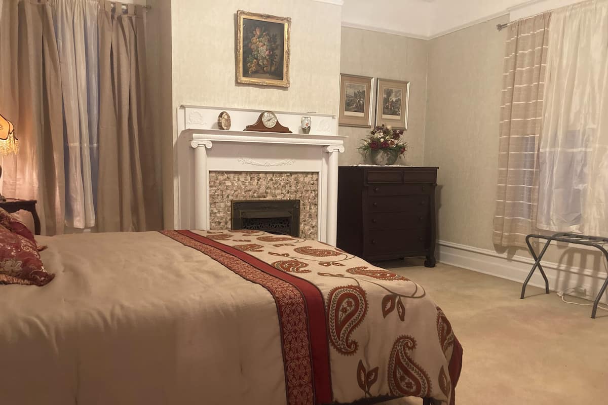 A bedroom with a bed, a fireplace, a dresser, and a chair.