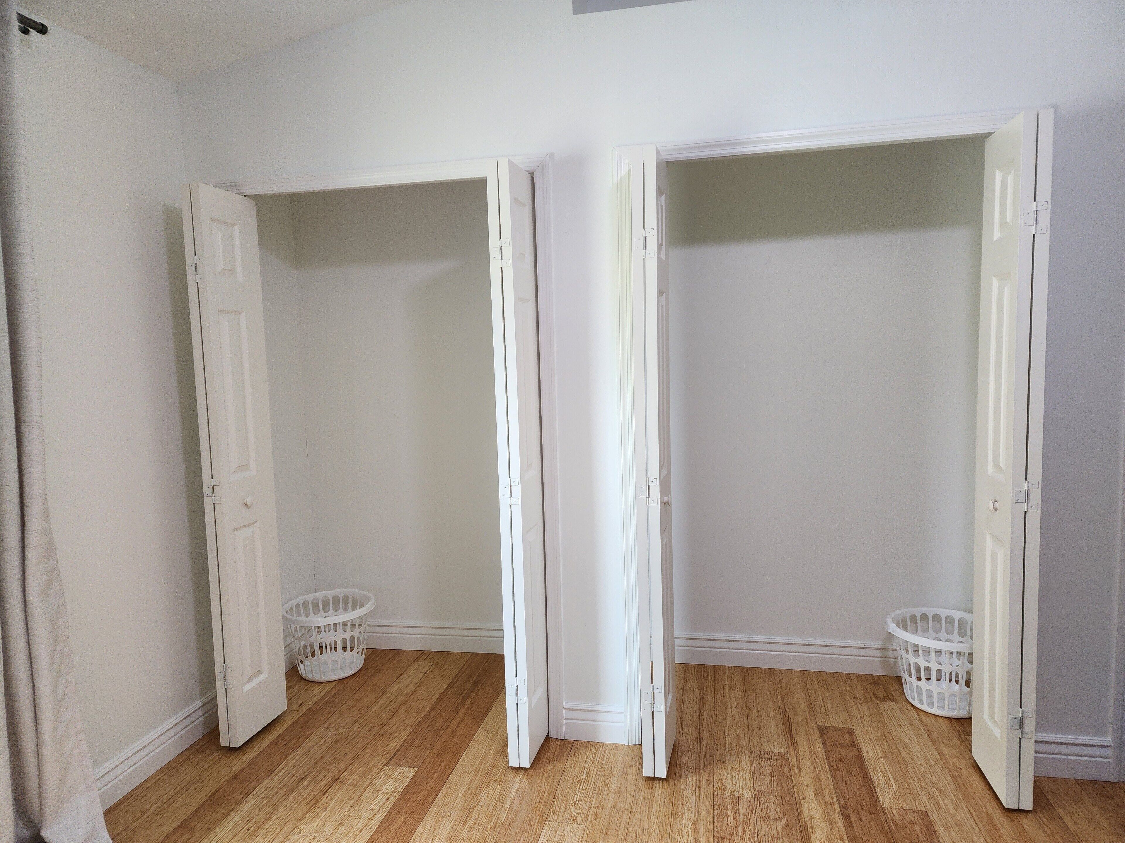 A room with two open closets and two white laundry baskets on a wooden floor.
