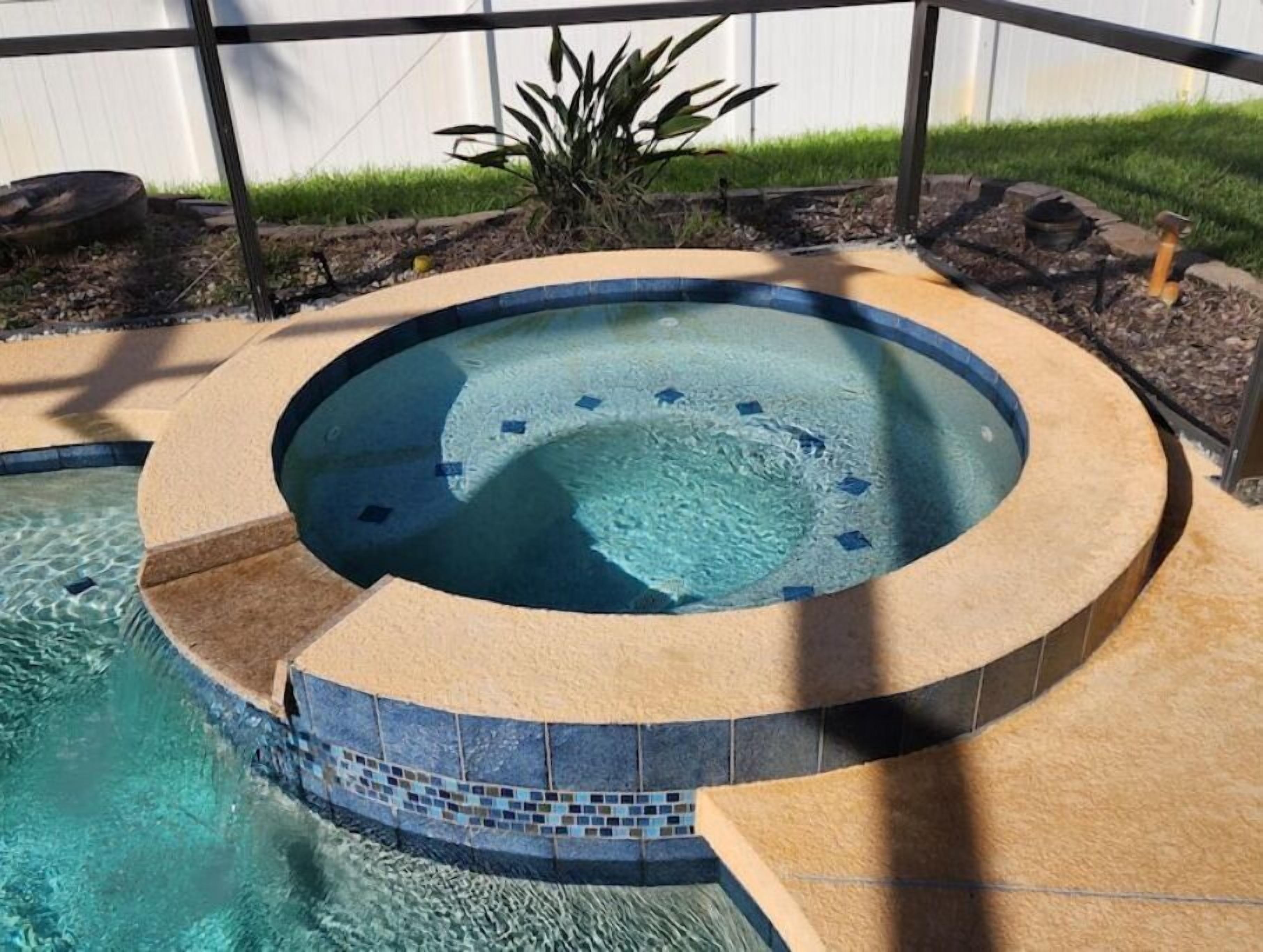A circular hot tub with a tiled edge, surrounded by a pool.