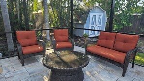 Uma varanda coberta com móveis de vime e uma mesa com tampo de vidro.
