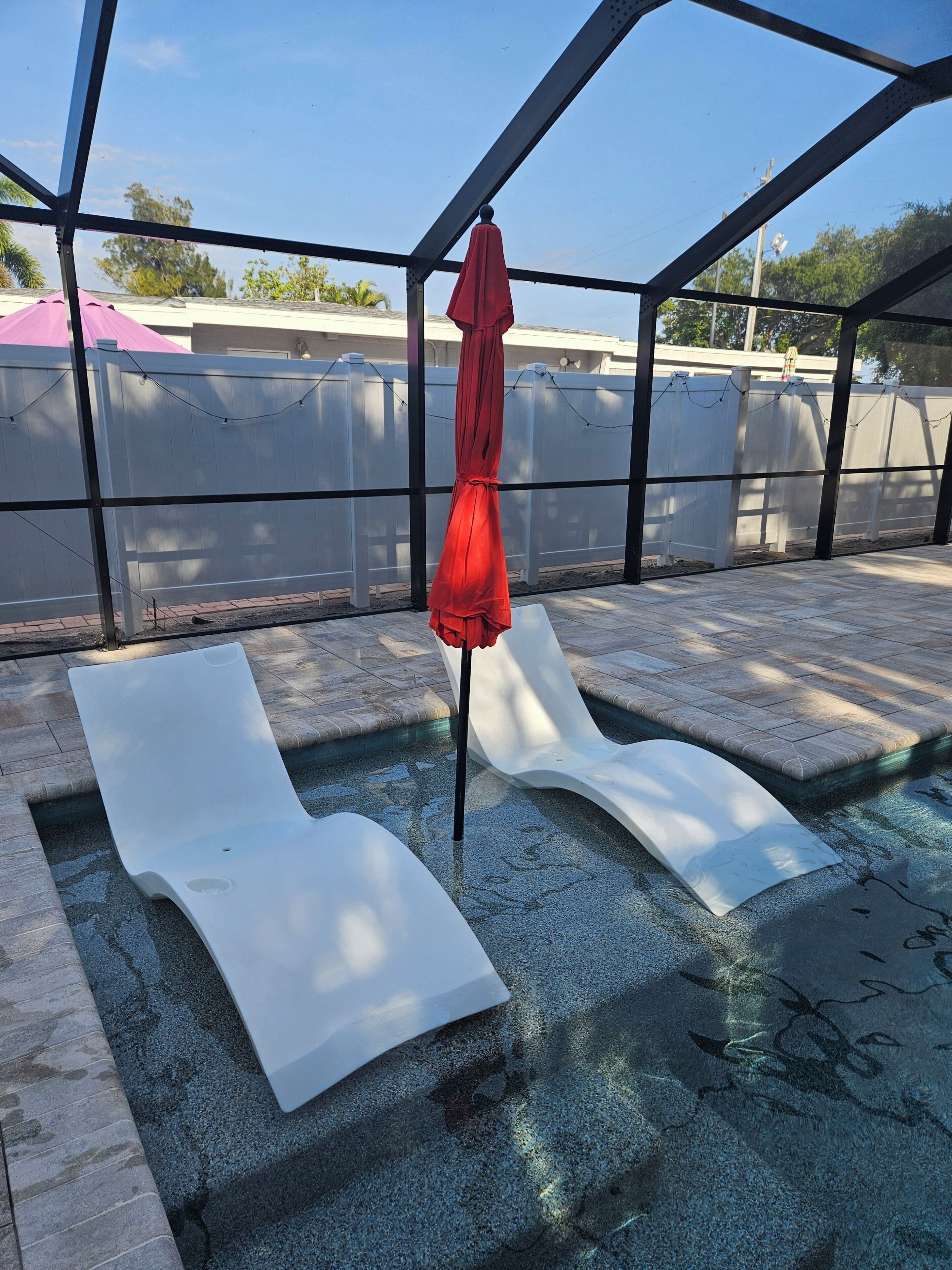 Une piscine avec deux chaises longues blanches et un parasol rouge.