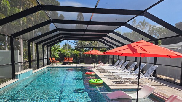 Piscina coberta com espreguiçadeiras e guarda-sóis, cercada por uma vedação e árvores.