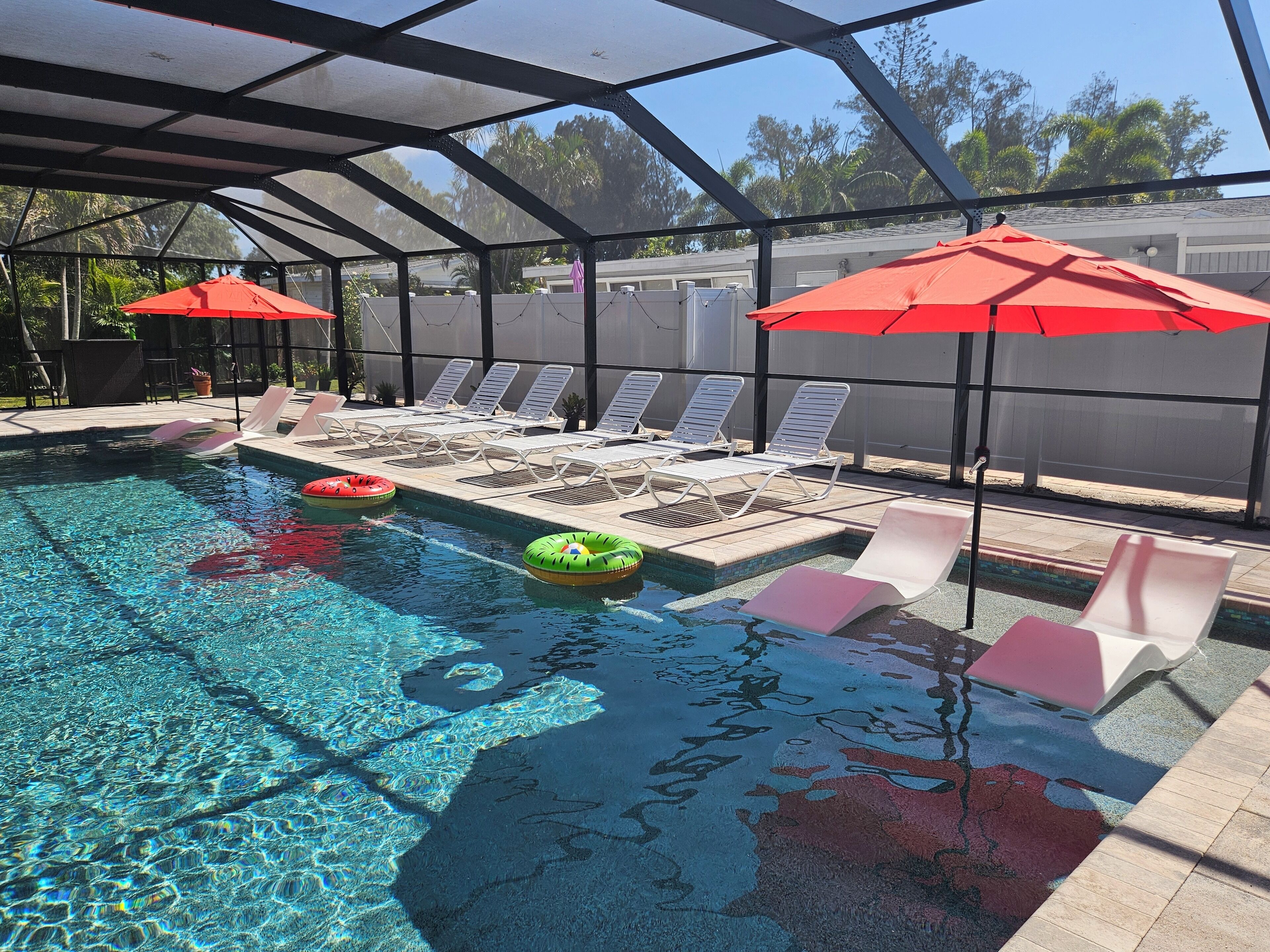 A swimming pool with clear water, lounge chairs, and red umbrellas.