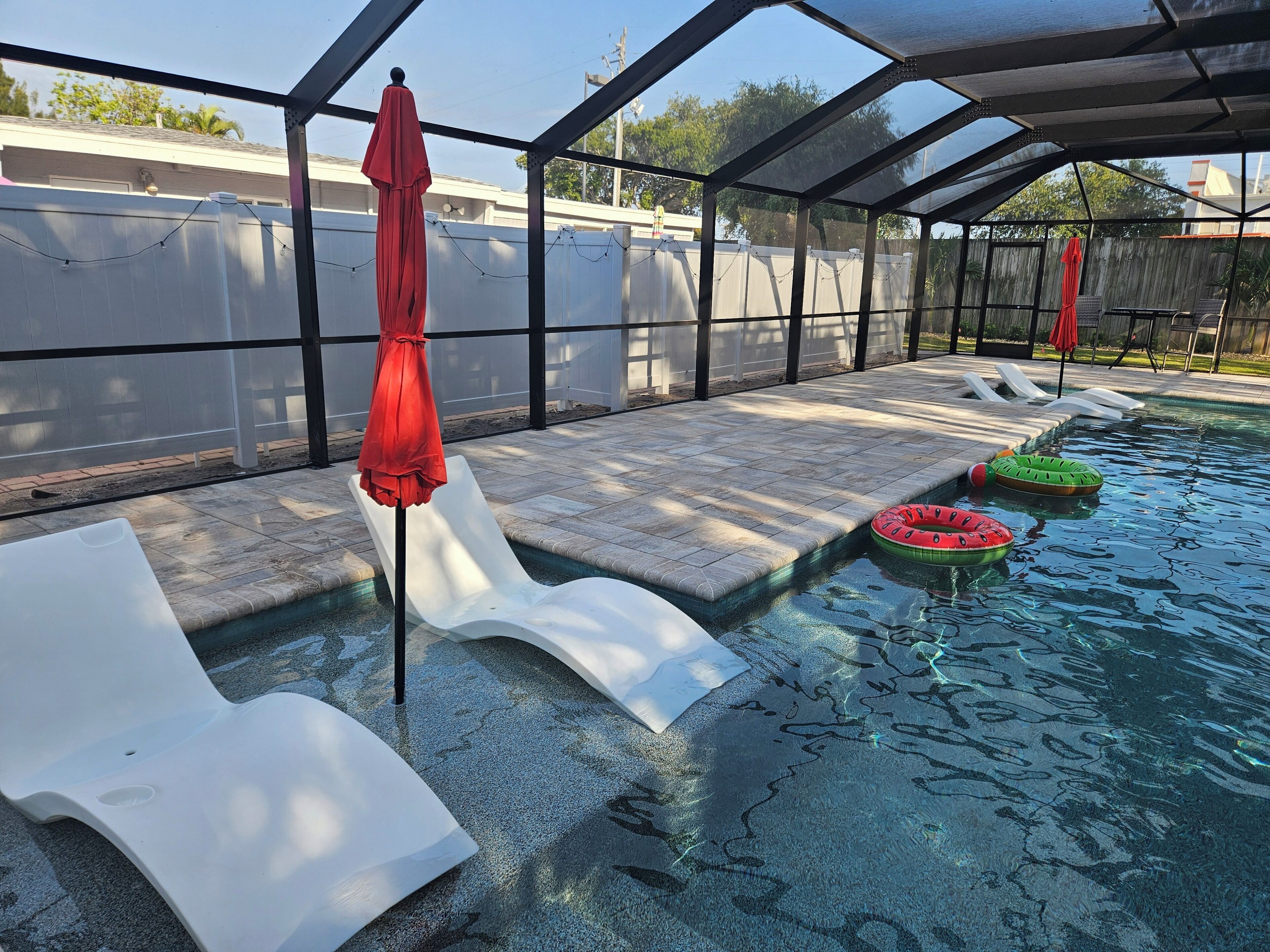 Ein Schwimmbecken mit klarem Wasser, umgeben von einer überdachten Terrasse mit Liegestühlen und Sonnenschirmen.