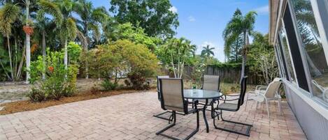 A patio with a brick floor, a table with chairs, and a view of tropical vegetation.