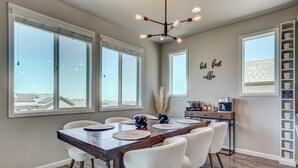 Un comedor con una mesa de madera, sillas blancas y ventanas amplias.