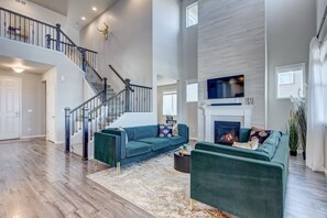 Un salón amplio con escalera, chimenea y un televisor grande montado en la pared.