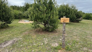 En skylt med texten ”Whispering Pines” placerad i en naturskön miljö med tallar och en grusväg.