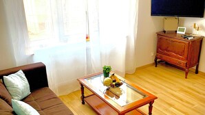 Una sala de estar con un sofá marrón, una mesa de centro de vidrio con fruta, un televisor sobre un mueble bajo y un aparador de madera.
