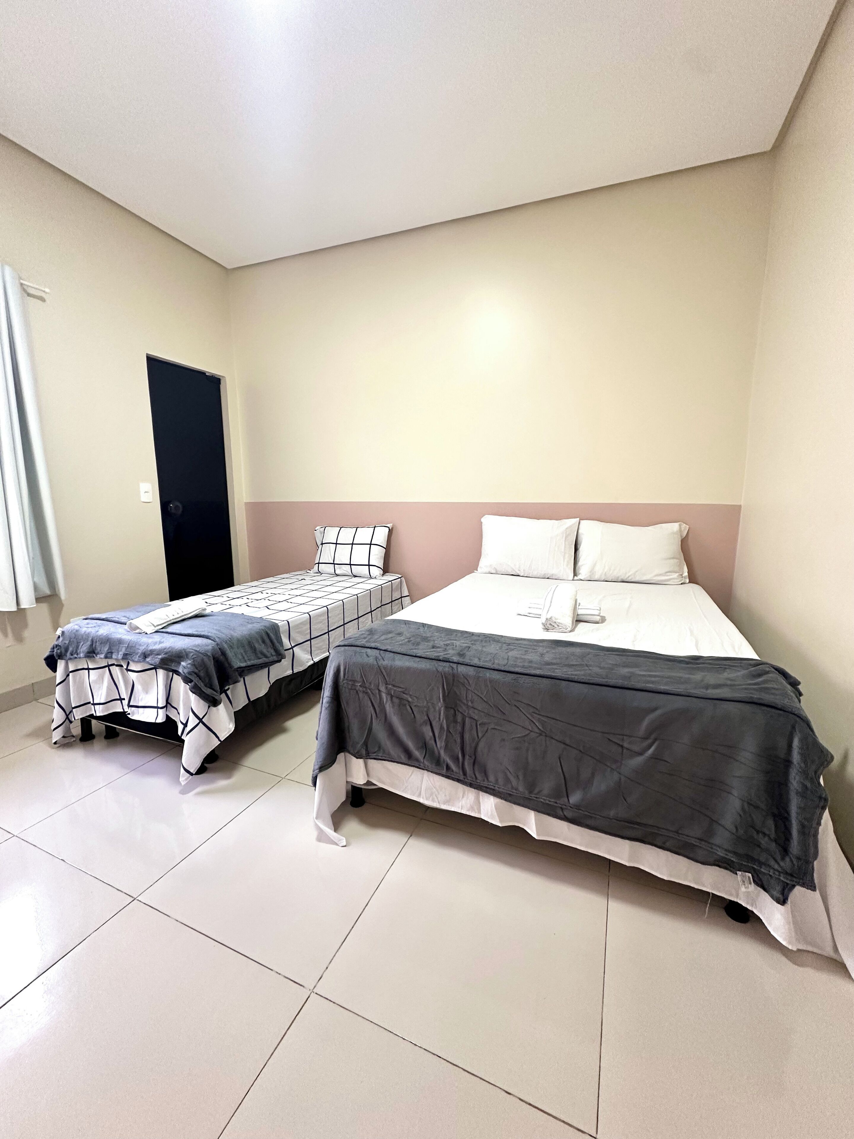 A bedroom with two beds, one larger and one smaller, both with plain bedding.