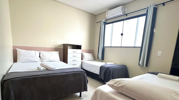 A hotel room with two beds, a window with curtains, a ceiling light, and a wall-mounted air conditioner.