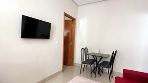 A modern living room with a flat-screen TV mounted on the wall, a dining table with chairs, a red sofa, and a fluffy rug.