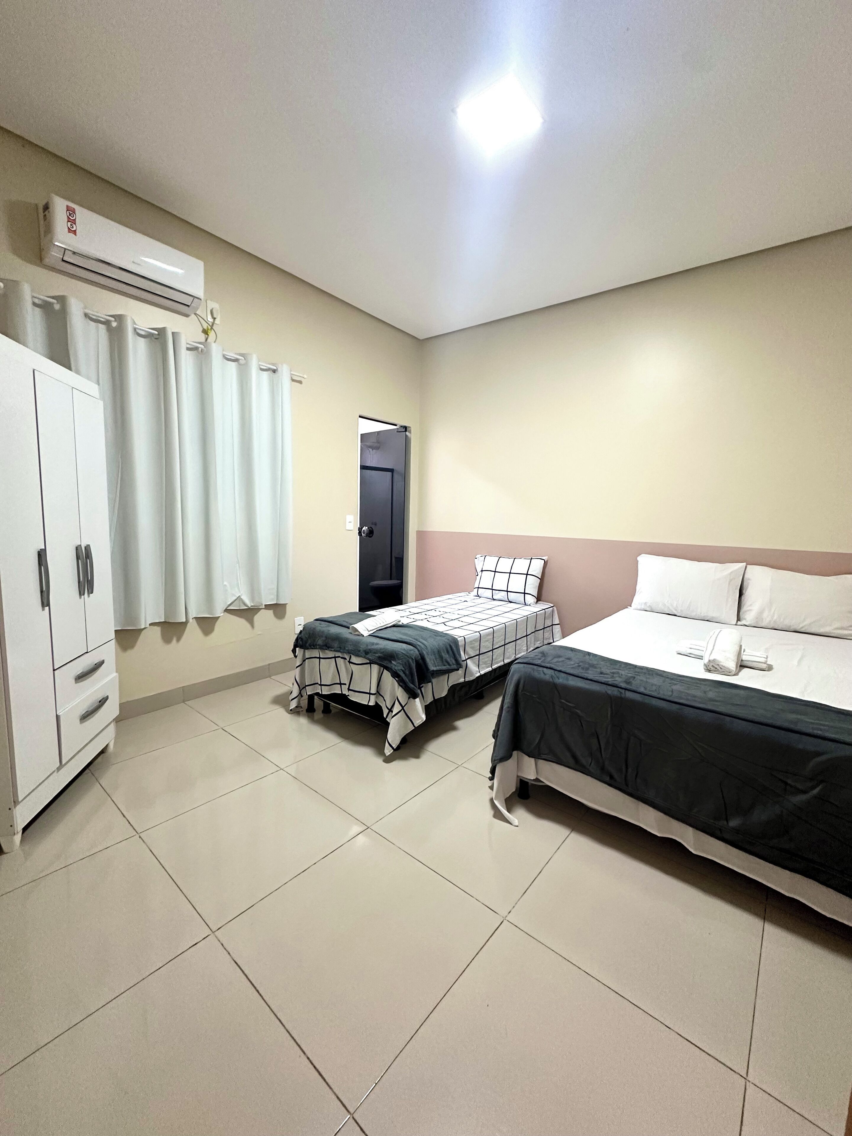 A hotel room with two beds, a wardrobe, a door, and an air conditioning unit.