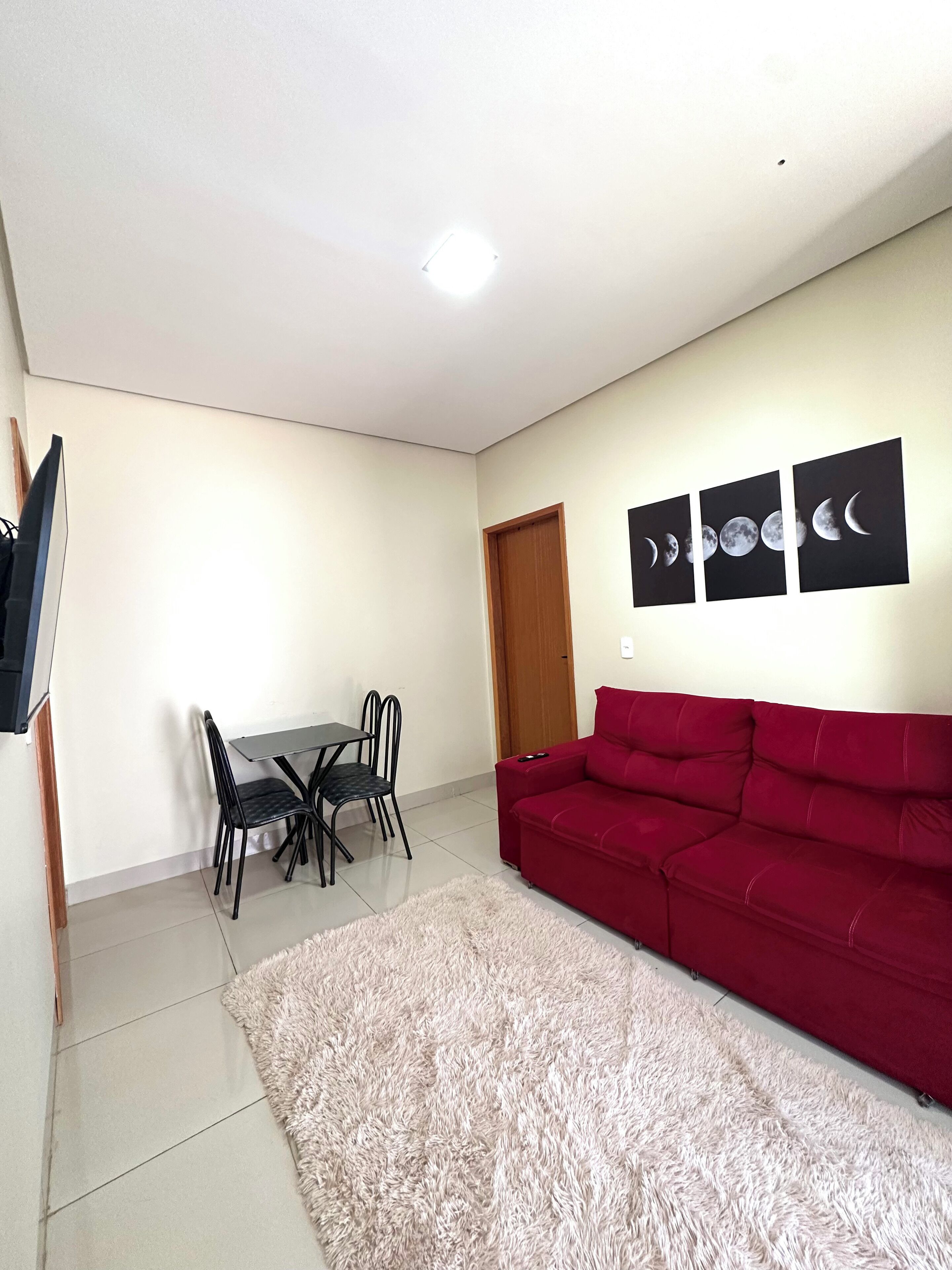 Un soggiorno con un divano rosso, un tavolo da pranzo con sedie, una TV e un muro decorato con arte raffigurante le fasi lunari.