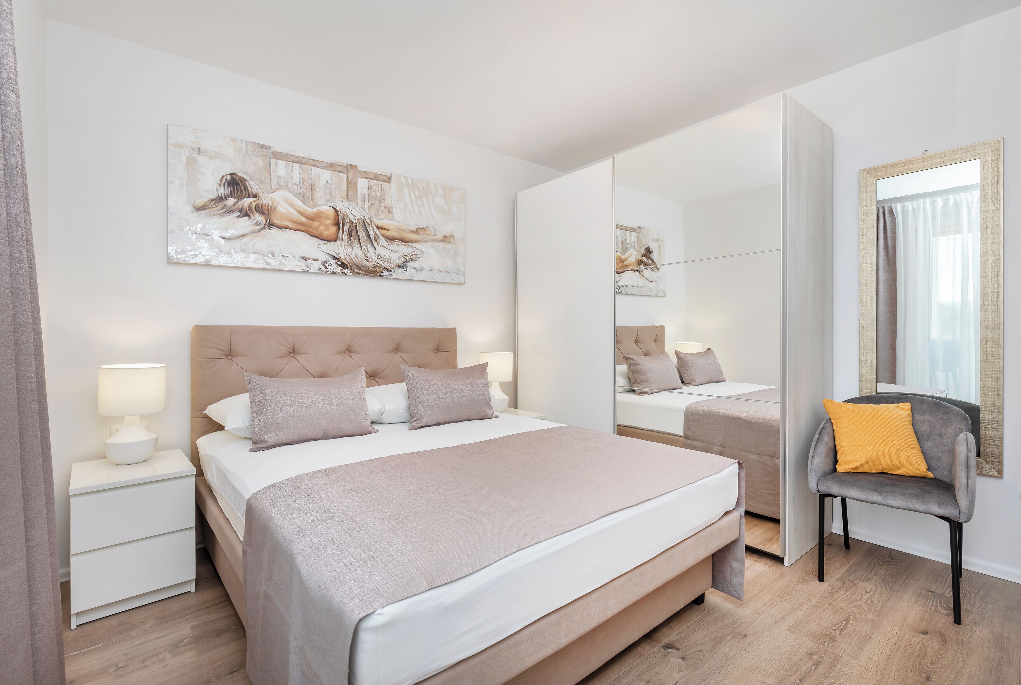 A modern bedroom with a large bed, bedside tables, a chair, and a painting on the wall.