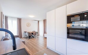 Une cuisine moderne dotée d’appareils électroménagers intégrés, un coin repas avec une table et des chaises, et un espace de vie comprenant un canapé et des rideaux.