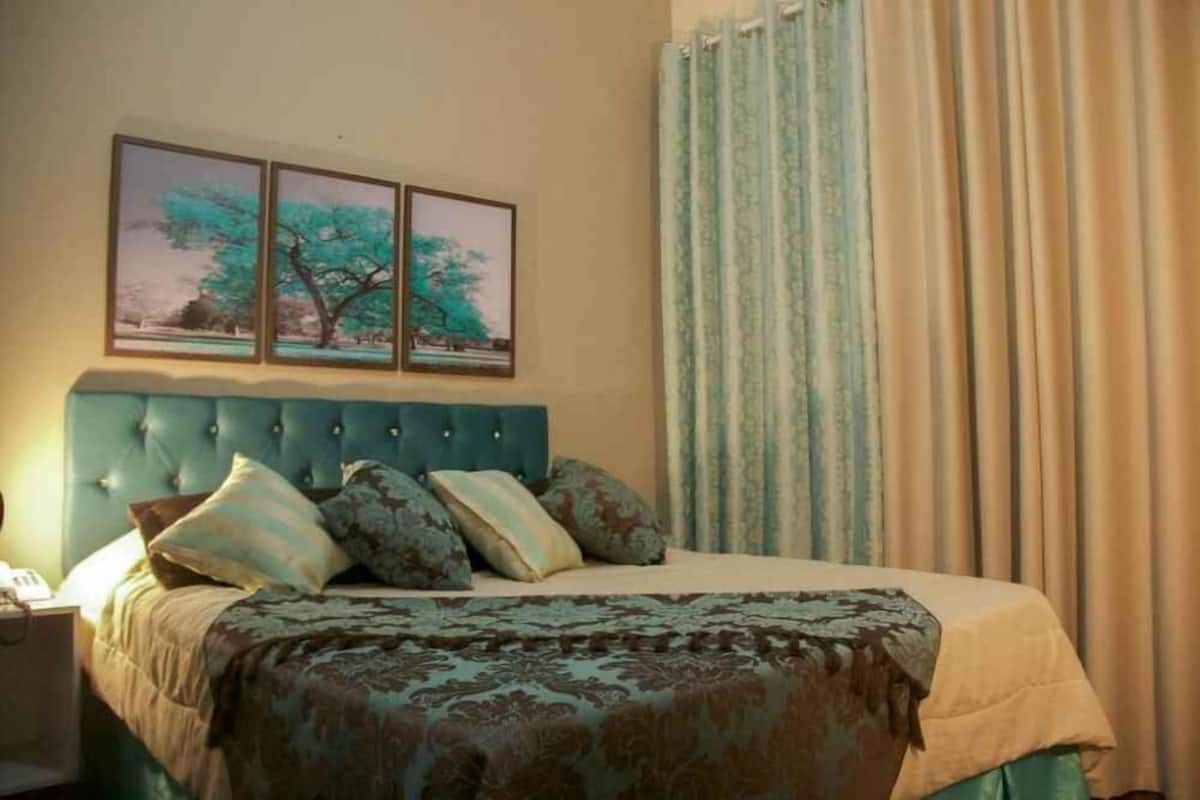A bedroom with a tufted headboard, a bed with patterned bedding, and three framed pictures on the wall.