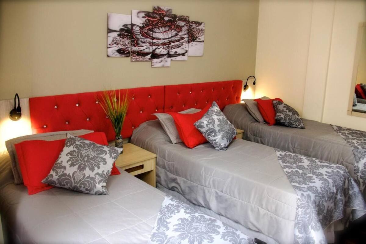 A hotel room with two beds, each with grey and red bedding, a red headboard, and a wall-mounted artwork above.