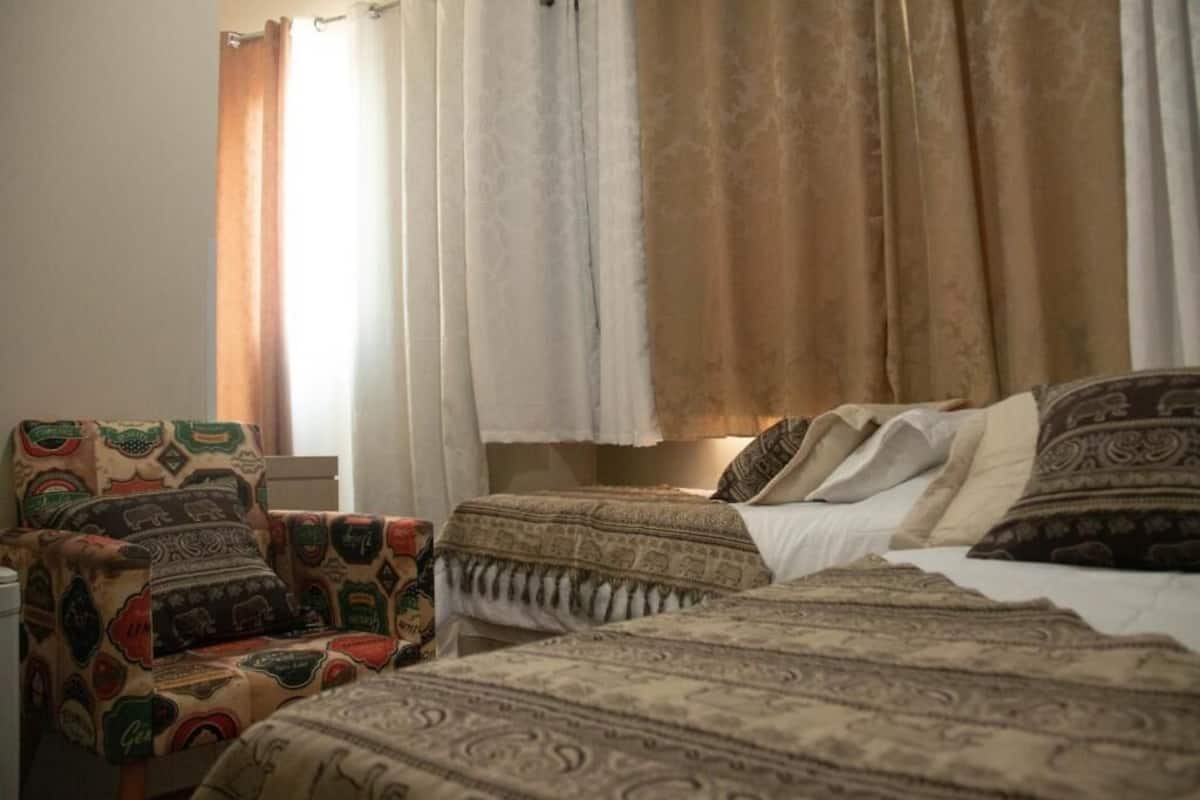 A room with two beds, a patterned armchair, and curtains.