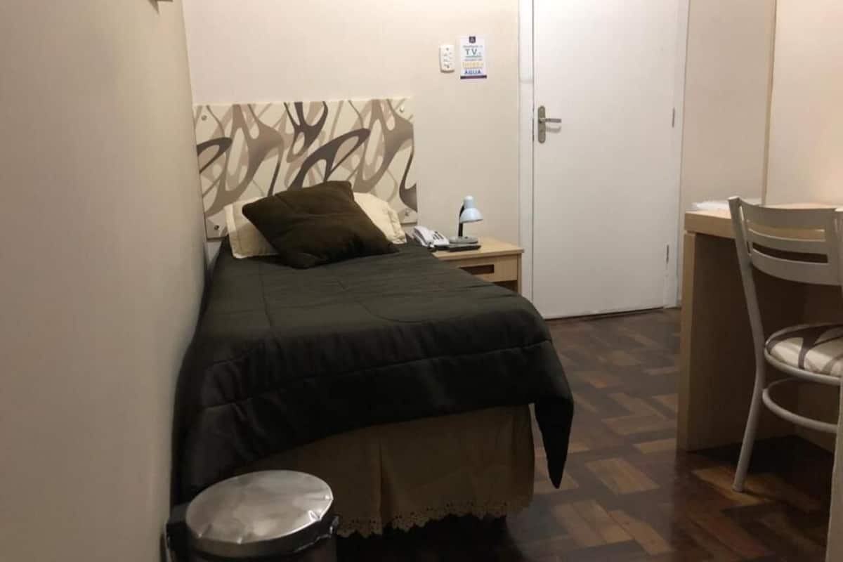 A bedroom with a bed, bedside table, lamp, and a chair.