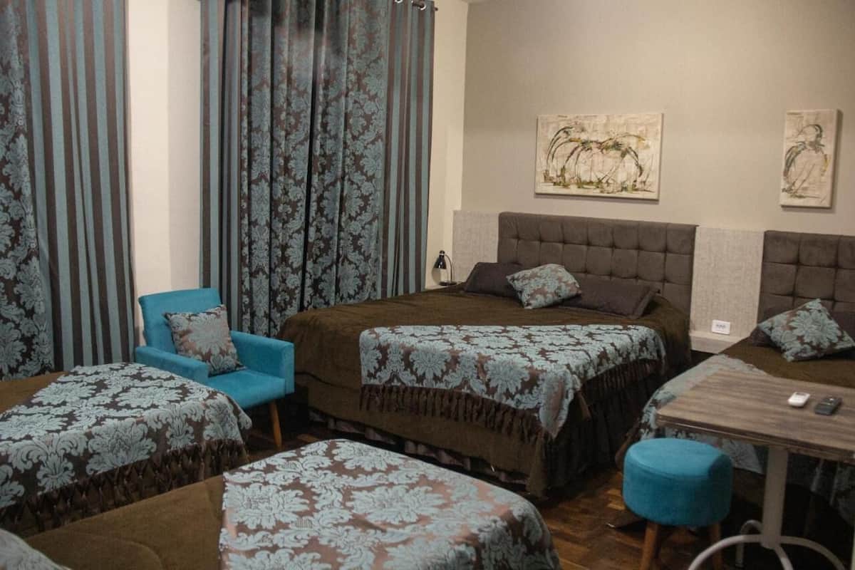 A hotel room with two beds, a chair, a table, and curtains.