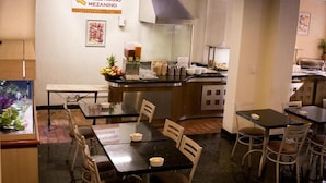 Un restaurante con mostrador, mesas y sillas para comer. Hay un letrero en la pared y una zona de cocina con estufa y utensilios.
