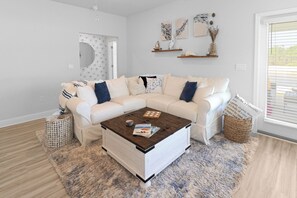 Un salon moderne avec un canapé d’angle blanc, une table basse en bois et un tapis à motifs.