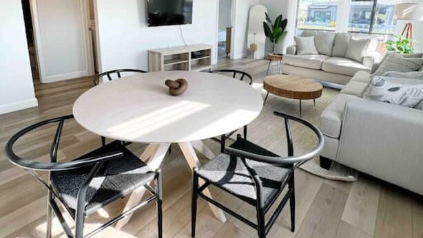 Una sala de estar moderna con una mesa redonda de comedor, sillas de metal negro, un sofá blanco y un ventanal grande.